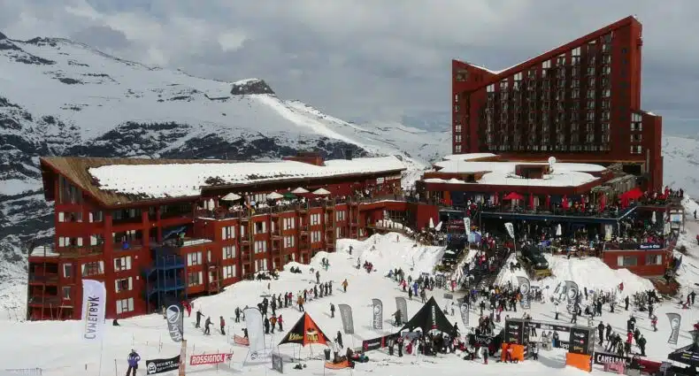 Imagem durante o dia de um hotel grande no centro e em volta coberto de neve. Representa o que fazer no Valle do Nevado.