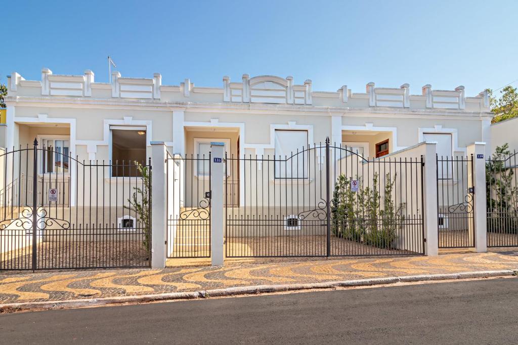 Fachada do Vila Brotas com um conjunto de três casas iguais. Cada uma apresenta duas janelas, uma escadinha que dá acesso a porta da frente, um jardim na parede e uma grade preta como portão. Imagem ilustrando post Airbnb em Brotas.