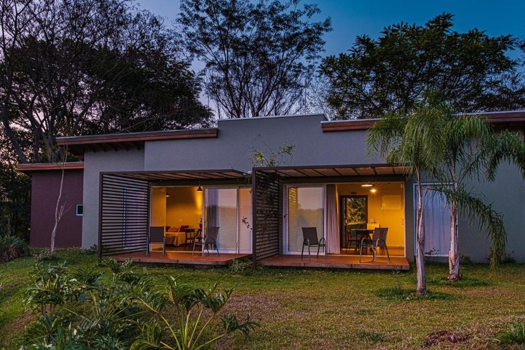 Fachada do Vila Poção como uma casa térrea com duas portas grandes de vidro que mostra a parte interna da casa e cada porta tem uma varanda com cadeiras com vista para as árvores ao redor. Imagem ilustrando post Airbnb em Brotas.