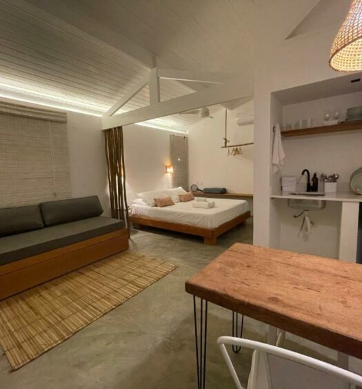 Estúdio do Villa Tennis. Uma mesa e uma mini cozinha do lado direito, do lado esquerdo um sofá cama, no fundo uma cama de casal. Foto para ilustrar post sobre airbnb no centro de Ubatuba.