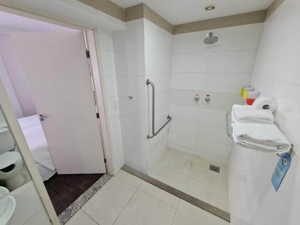 Banheiro acessível em Wafeh Flats San DIego. O espaço é largo,  área da ducha contém barras de apoio. O banheiro não está visível neste ângulo, mas também é acessível. A porta está entre a pia e a ducha, na esquerda.