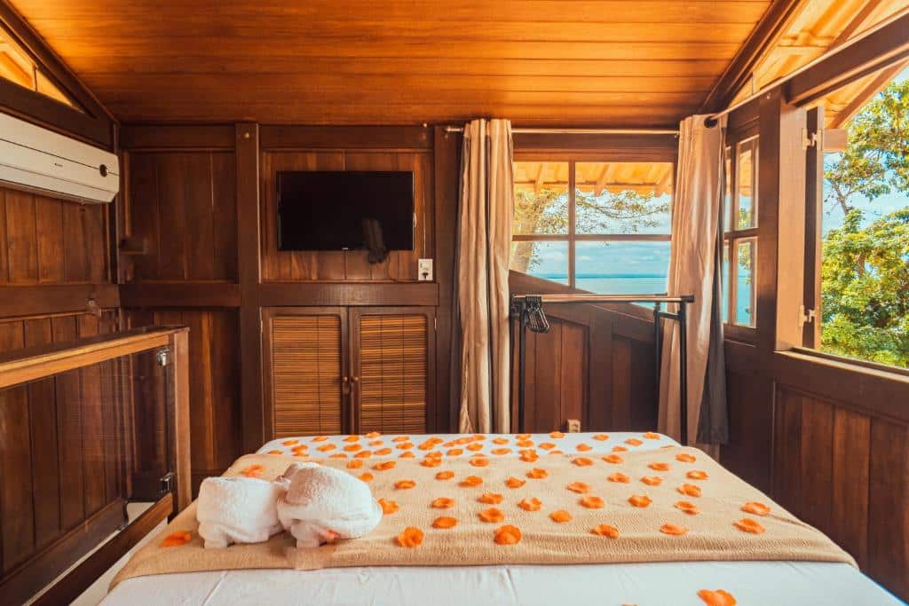 Quarto da Altavista residence. Uma cama de casal no meio, de frente uma televisão e um cabideiro. Na frente e do lado direito uma janela com vista do mar. Do lado esquerdo o ar-condicionado. Foto para ilustrar post sobre airbnb em Morro de São Paulo.