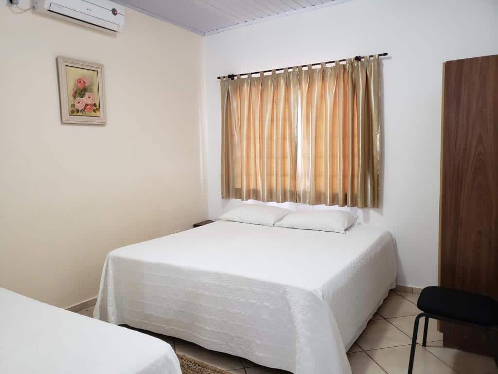 Quarto do Angel Family Houses. Há uma cama de casal no centro, uma janela atrás, um guarda-roupa e uma cadeira à direita e um ar-condicionado na parede à esquerda da cama. Está ilustrando o post sobre airbnb em Foz do Iguaçu.