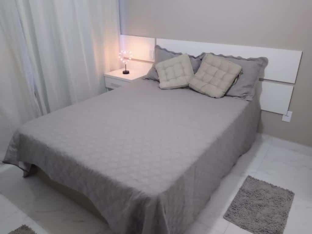 QUarto do Apartamento Praia do Forte VIP. A cama está centralizada no quarto e no lado esquerdo da cama há uma pequena cômoda com um abajur. Imagem para ilustrar o post airbnb em Cabo Frio.