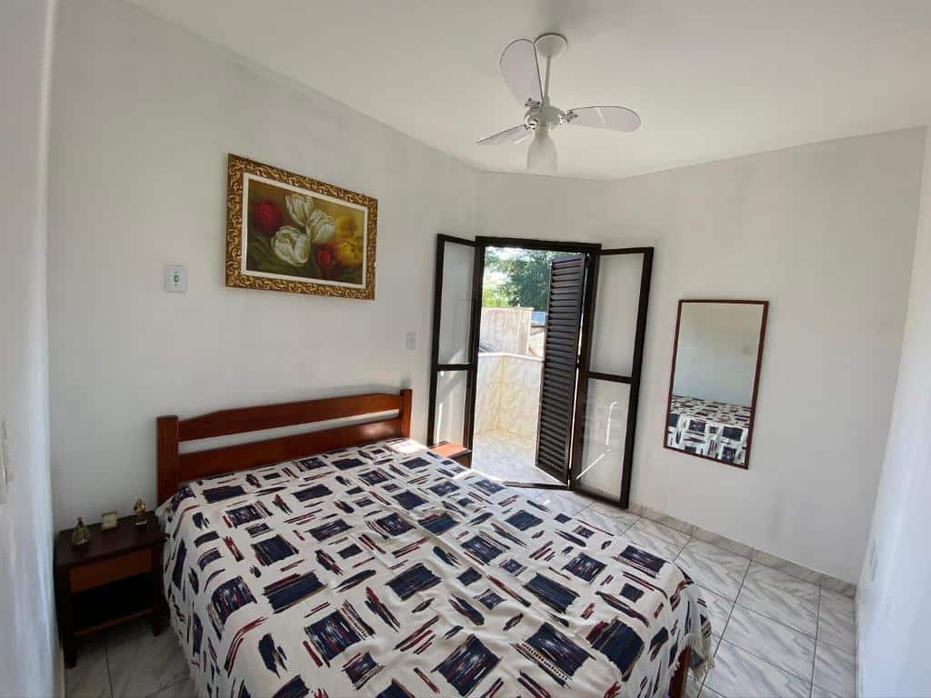 Quarto do Apartamento Ubatuba, Itaguá. Do lado esquerdo uma cama de casal, de cada lado uma cômoda. No fundo, no lado direito um espelho, no lado esquerdo a porta da sacada.