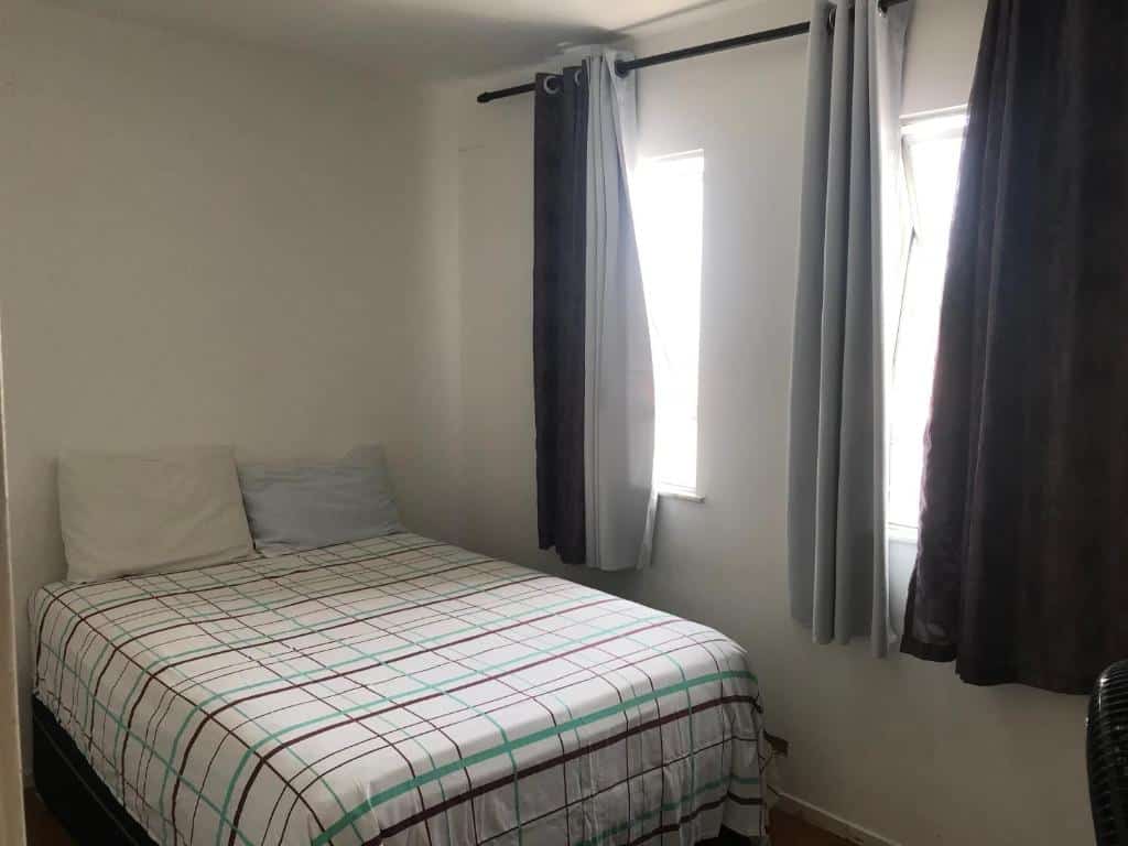 Quarto do Apto Praia Atalaia. Uma cama de casal do lado esquerdo, do lado direito duas janelas com cortinas. Foto para ilustrar post sobre airbnb em Aracaju.