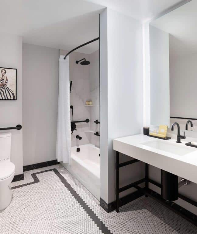 Banheiro com mobilidade do The Clift Royal Sonesta San Francisco com pia do lado direito a frente ao fundo área do chuveiro com barras de apoio e do lado esquerdo vaso sanitário com barras de apoio.