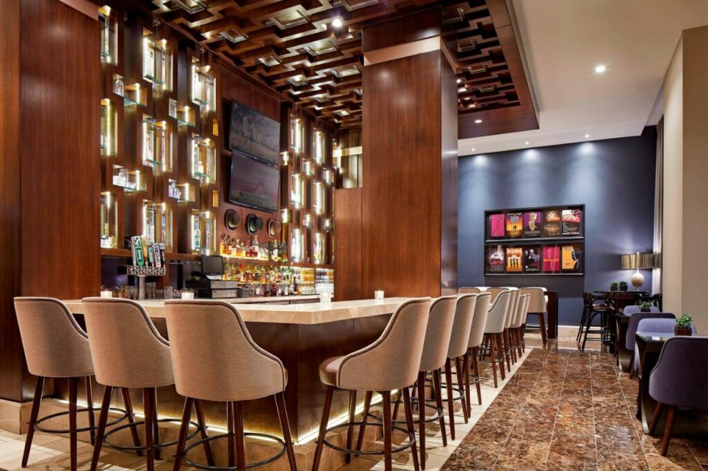 Bar do Hotel Adagio, Autograph Collection com cadeiras a frente em volta do balcão.