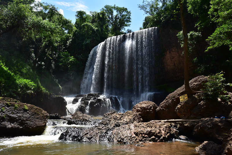 Cachoeira Astor com uma quadra livre de água grande e várias pedras e árvores verdes e grandes em volta durante o dia, ilustrando post Airbnb em Brotas.