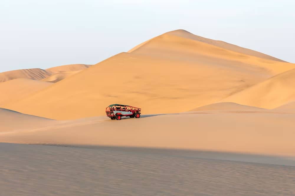 Buggy andando em meio ao Deserto de Huacachuna. O deserto tem montanhas de areia e o raio do sol amarelado refletindo nelas. Foto: Civitatis