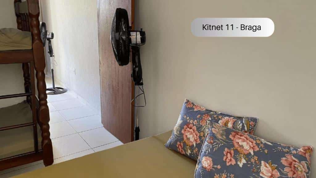 Quarto do Cabo Frio - Braga - Kitnets - Aluguel Econômico. No canto direito é possível ver parte de uma cama de casal, no canto esquerdo é possível ver parte de uma beliche, na frente um ventilador de chão e uma porta. Imagem para ilustrar o post airbnb em Cabo Frio.