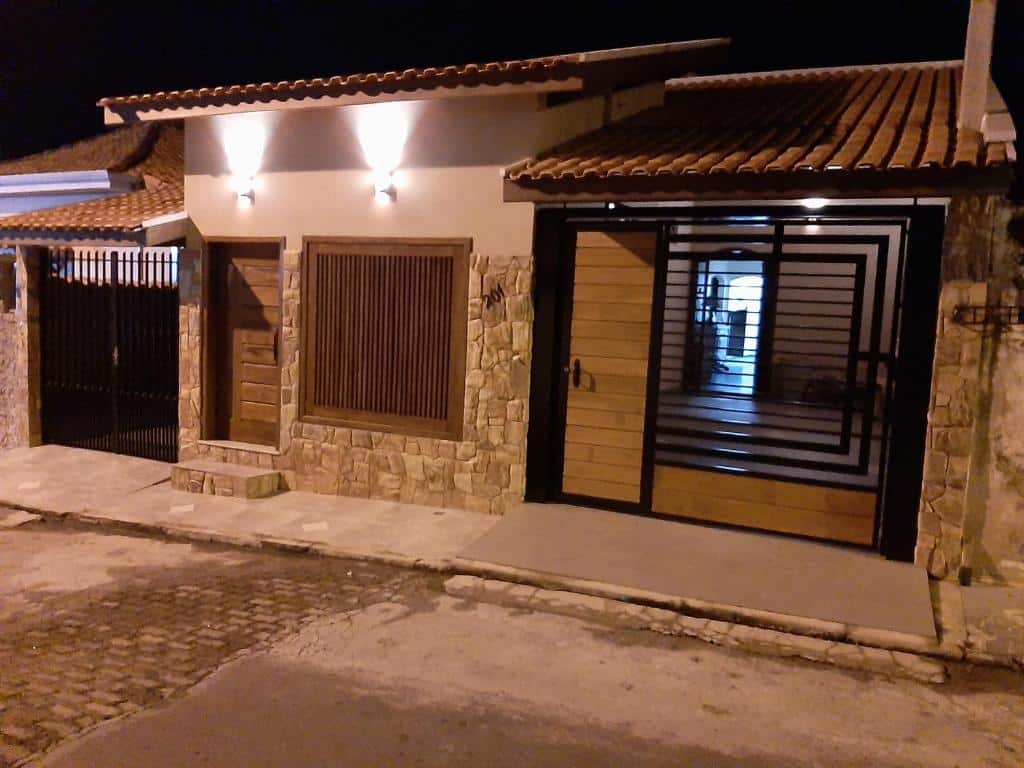 Fachada do Cantinho Cunhense que mostra dois terrenos pequenos em uma casa só. A fachada tem um portão e duas portas, a parede tem detalhes em pedra e a casa tem uma garagem. Imagem ilustrando post Airbnb em Cunha.