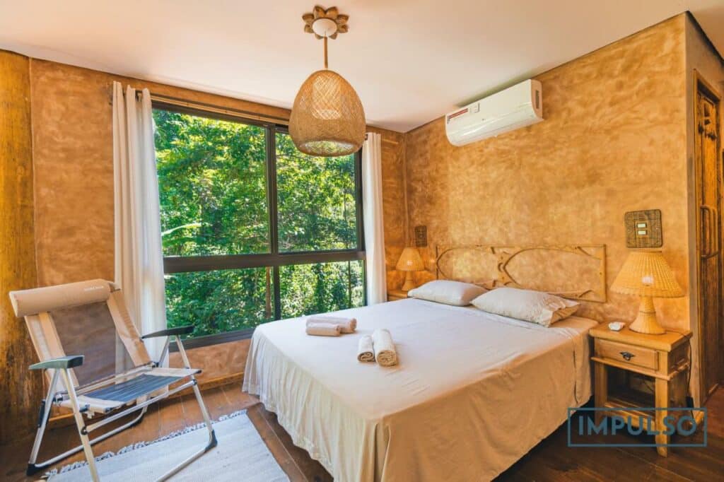 Quarto da Casa Eleva a 200 mts da praia Félix com cama de casal do lado direito da imagem com uma cômoda de cada lado com luminária, em frente a cama do lado esquerdo uma cadeira.