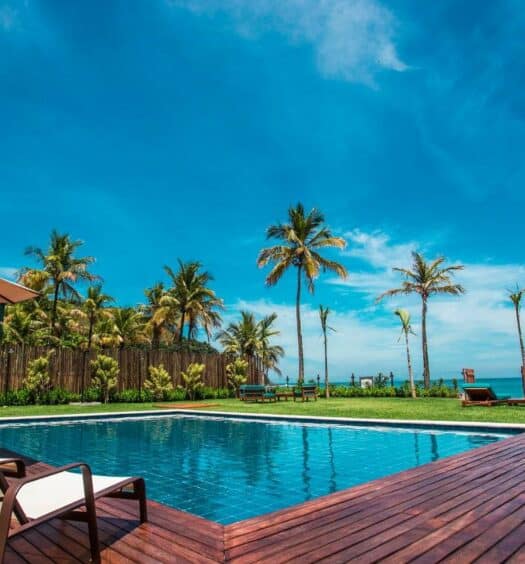 Piscina do Residencial Marina Del Sol durante o dia com cadeiras do lado esquerdo da imagem, no centro em frente a piscina. Representa airbnb na praia de Calhetas