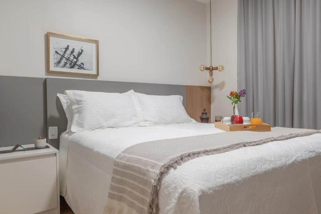 Quarto da Casa Caju. Uma cama de casal no meio, de cada lado uma cômoda, em cima da cama uma mesa de madeira com xícaras e sucos. No fundo um lustre. Foto para ilustrar post sobre airbnb em Aracaju.