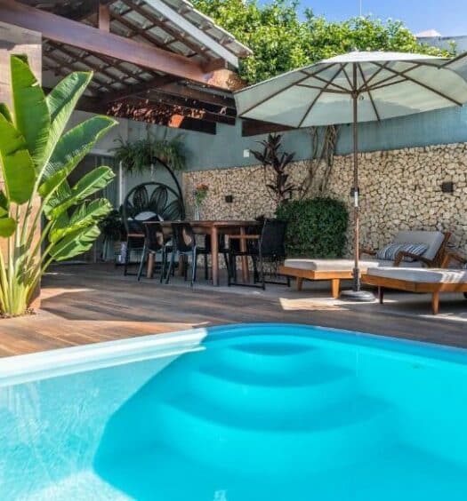 Área externa da Casa Caju para ilustrar post sobre airbnb em Aracaju. Na frente uma piscina, no fundo cadeiras de tomar sol, mesa e cadeiras com guarda-sol.
