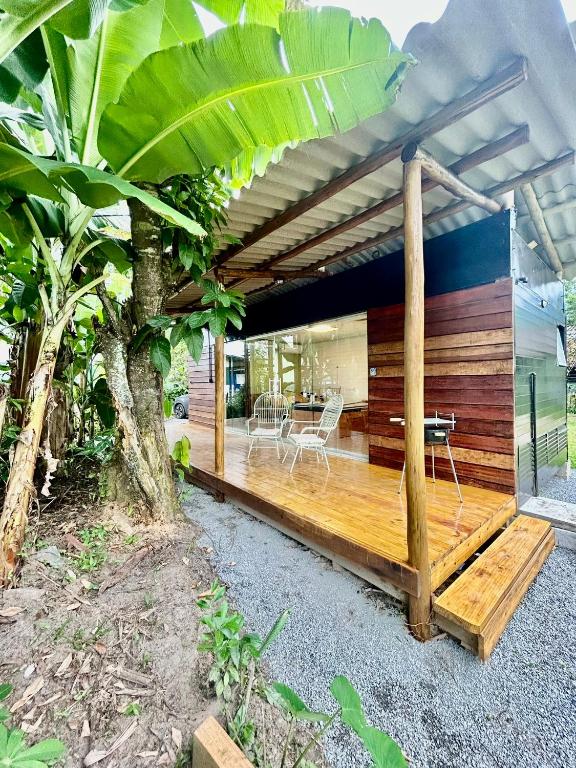 Área externa da Casa do bananal. Uma varanda de madeira com duas cadeiras e uma churrasqueira elétrica.