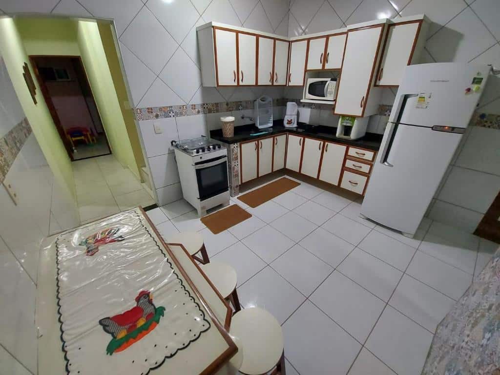 Cozinha da Casa inteira em Fortaleza com 02 Quartos sendo 01 Suíte - Praia do Futuro. Um grande armário está embutido na parede e ao lado do fogão e da geladeira. É possível ver também um micro-ondas. Na outra parede há uma mesa e alguns bancos.