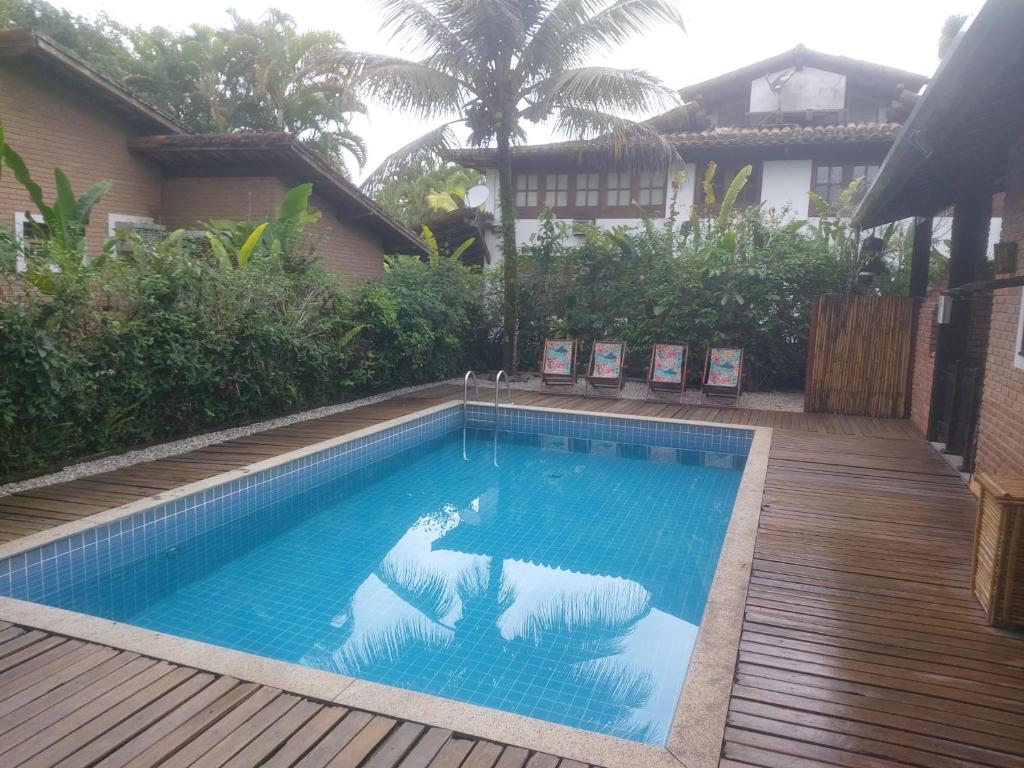 Área externa da Casa na praia de Itamambuca. Uma piscina no meio, no fundo cadeiras de madeira, ao redor um cercado de plantas.