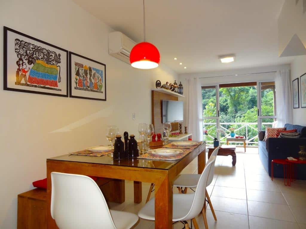 Sala de estar da Casa Verde e Mar. Na frente há uma mesa retangular com pratos, taças e cadeiras em volta e ao fundo está o sofá, TV e varanda. Imagem para ilustrar o post airbnb em Angra dos Reis.