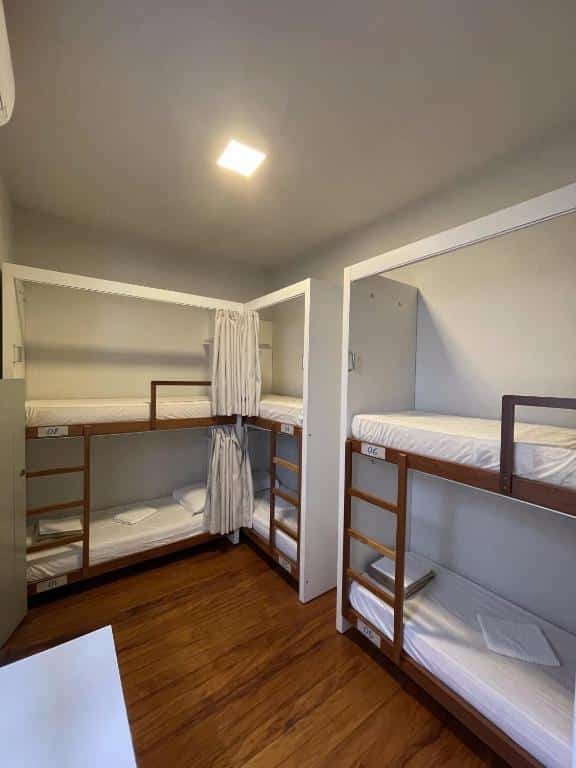 Quarto do Casarão Hostel com seis camas em formato de beliche. Todas possuem roupa de cama e uma cortina. Imagem ilustrando post Airbnb em Capitólio.