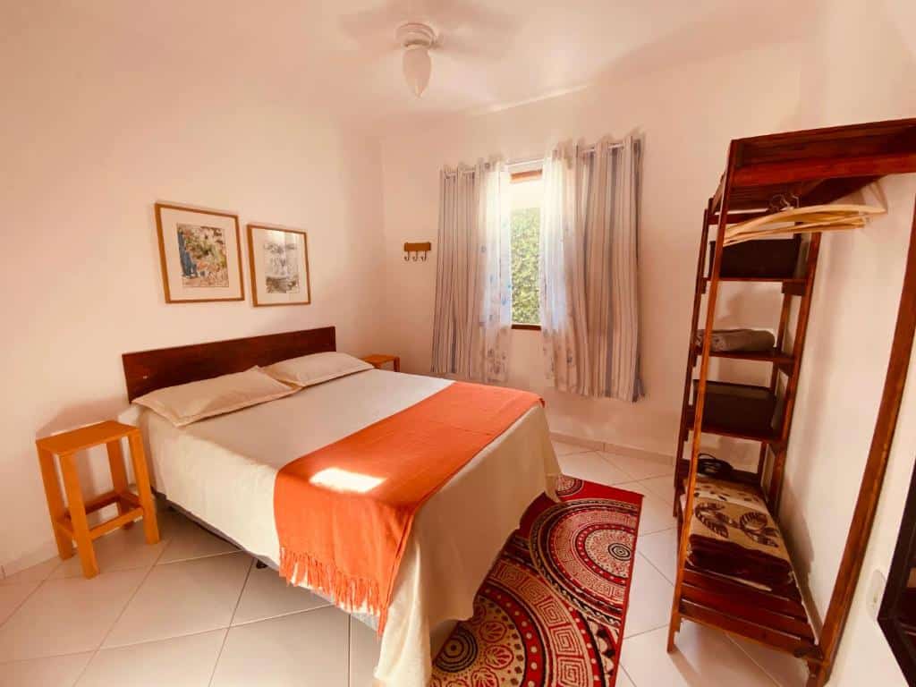 Quarto da Casas Aconchegantes Temporada. A cama de casal está no lado esquerdo, em cada lado da cama há uma pequena mesinha e na frente da cama há um armário. Imagem para ilustrar o post airbnb em Cabo Frio.