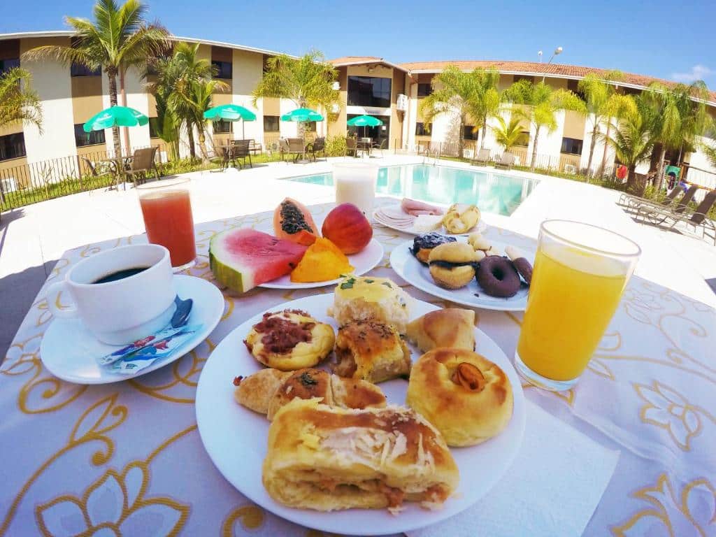 Um café da manhã numa mesa à beira da piscina no Cegil Hotel Boulevard. Na mesa vemos pratos com doces, massas e frutas e copos com suco, e também uma xícara de café.