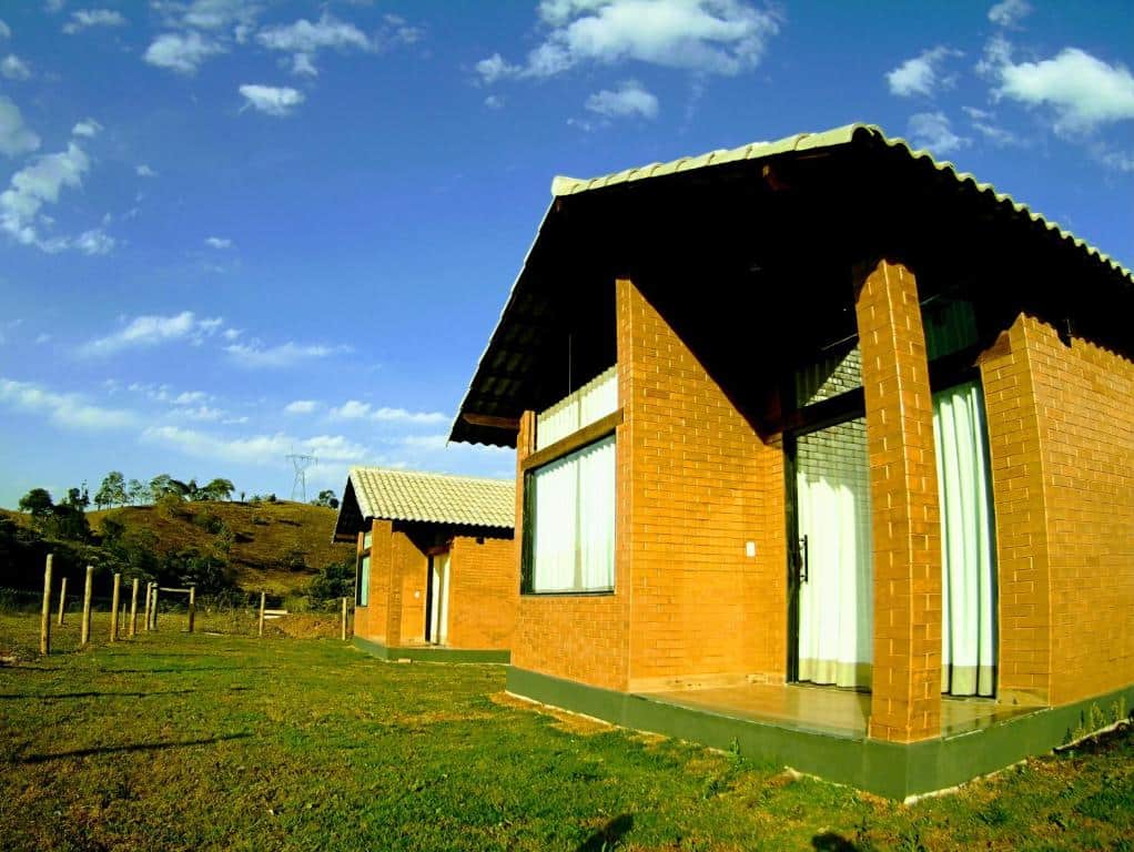 Fachada dos Chalés Estância Campestre que mostra dois chalés de tijolos a vista com portas e janelas de vidro em volta de um amplo gramado verde. Imagem ilustrando post Airbnb em Capitólio.