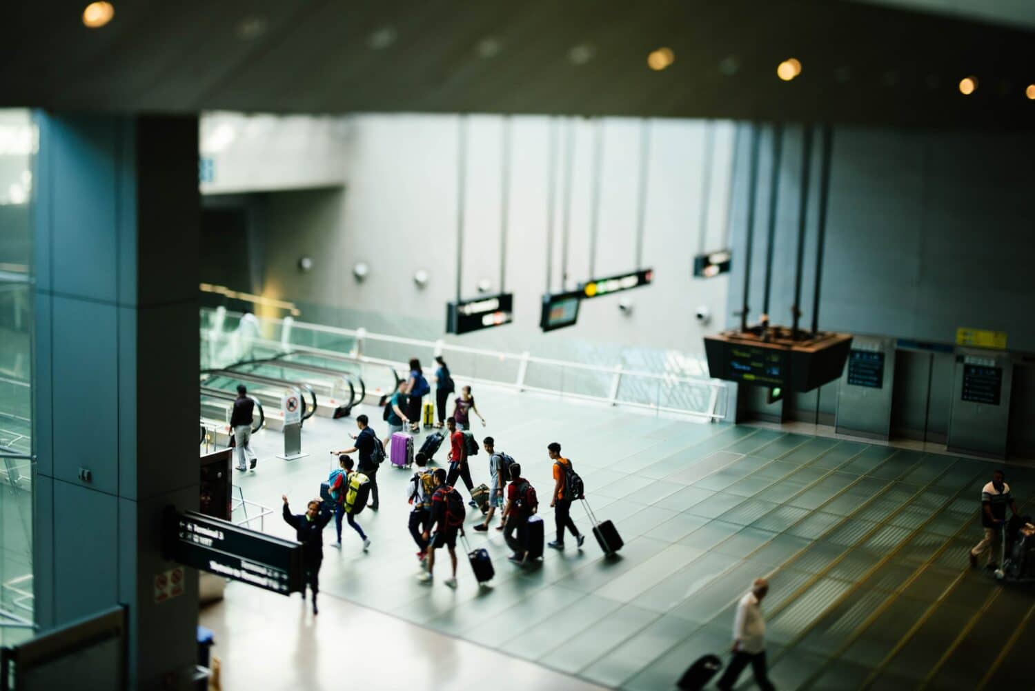 Um aeroporto com pessoas andando com malas de viagem em direção de escadas rolantes, para representar seguro viagem anual