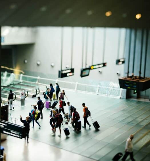 Um aeroporto com pessoas andando com malas de viagem em direção de escadas rolantes, para representar seguro viagem anual