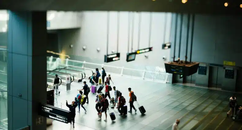 Um aeroporto com pessoas andando com malas de viagem em direção de escadas rolantes, para representar seguro viagem anual