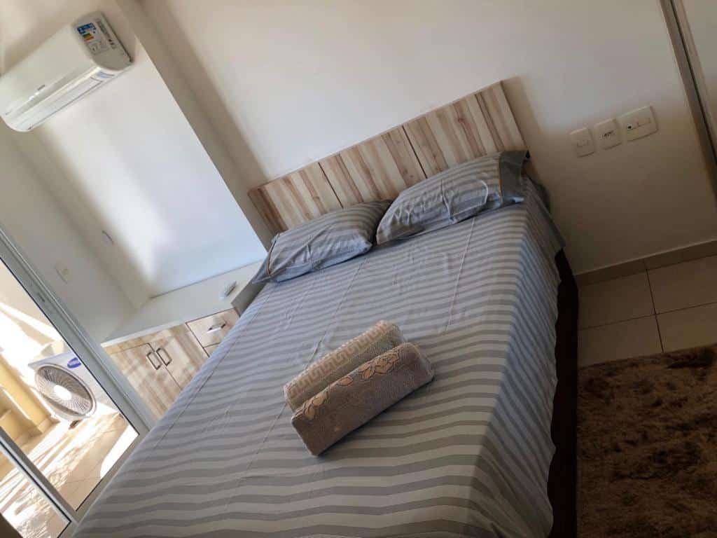Um dos quartos do Condomínio Bech Village praia do futuro fortaleza. Uma cama está no meio do quarto, com duas toalhas em cima dela. Ao seu lado há umma cômoda e um ar-condicionado. Do outro lado existem tomadas na parede.