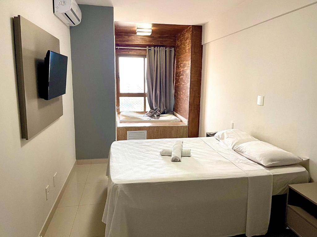 Quarto do Duplex com Hidromassagem. Uma cama de casal do lado direito com uma cômoda de cada lado, de frente uma televisão. No fundo uma banheira de hidromassagem com uma janela. Foto para ilustrar post sobre airbnb em Aracaju.