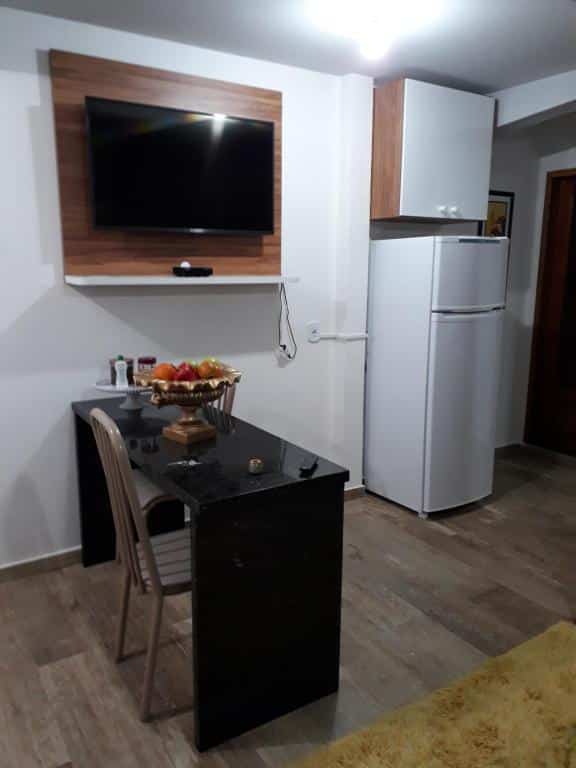 Parte do Espaço Kayan que mostra uma bancada de pedra mármore preta com uma cadeira, em cima na parede uma tv e ao fundo uma geladeira com um armário. Imagem ilustrando post Airbnb em Cunha.