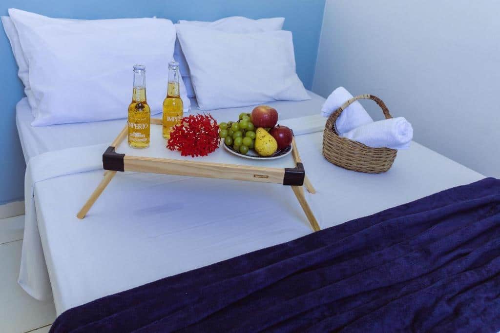 Quarto do Flat com 2 quartos. Uma cama de casal, em cima uma mesa de madeira com pratos com frutas e duas cervejas, do lado uma cesta de palha com toalhas. Foto para ilustrar post sobre airbnb em Aracaju.
