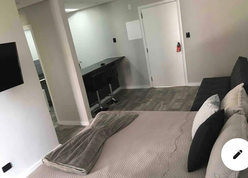 Quarto do Flats São Vicente. Uma cama de casal do lado direito com um sofá cama. De frente uma televisão e um balcão. Foto para ilustrar post sobre pousadas em São Vicente.