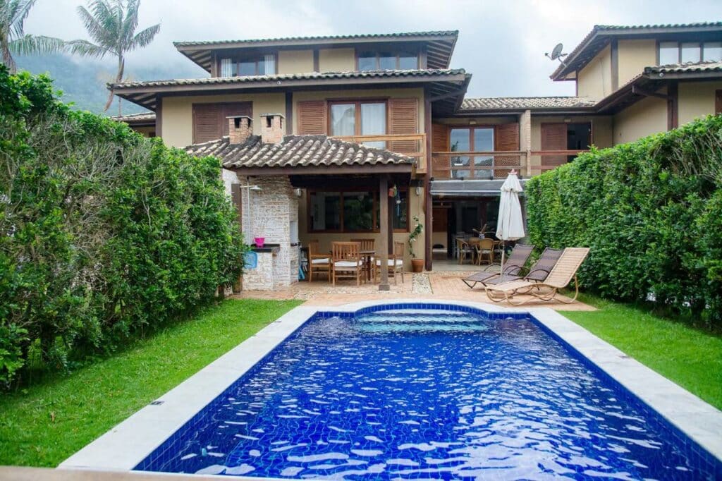 Frente da Incrível casa pé na areia com Wi-Fi em Guaeca-SP durante o dia com piscina a frente e ao fundo a estadia.