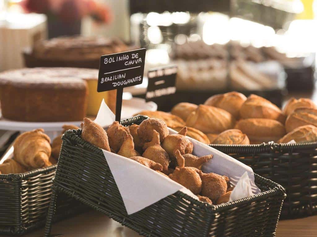 Buffet de café da manhã do ibis Styles Taubaté. Há várias cestas com bolinho de chuva, doces, pães, bolos, etc.