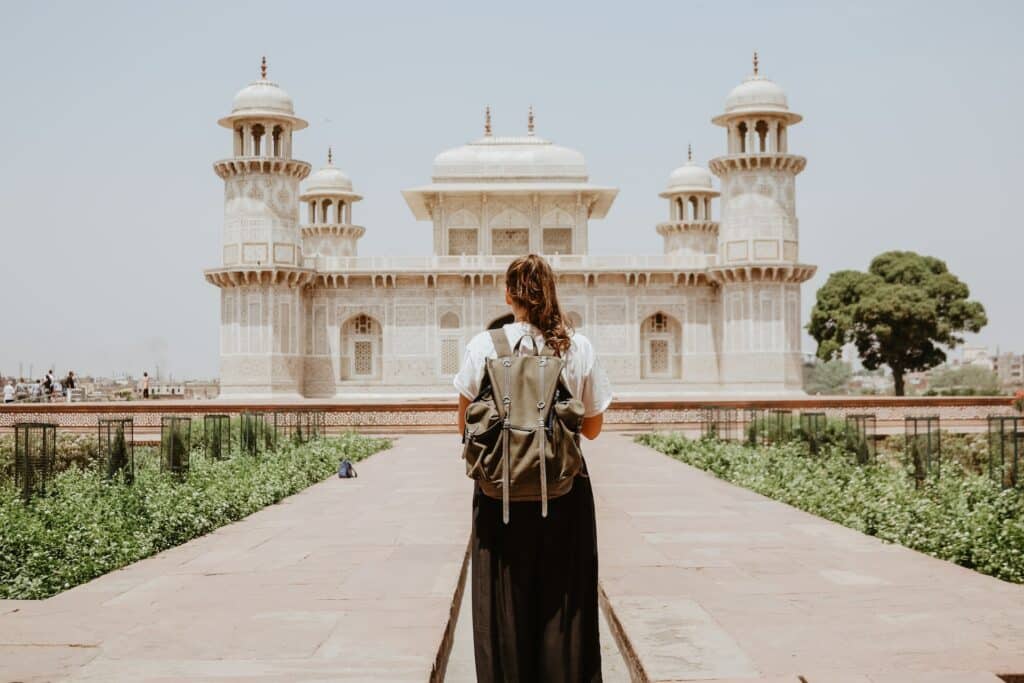 Uma mulher com uma mochila nas costas parada em frente há uma construção histórica no formato de templo em Agra na Índia