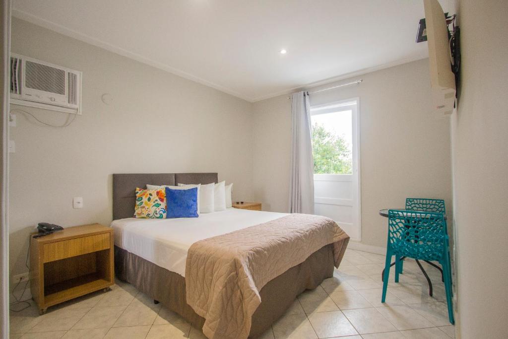 Quarto da Ilha Porchat Hotel. Do lado direito uma televisão e uma mesa com duas cadeiras. Do lado esquerdo uma cama de casal com uma cômoda de cada lado. Foto para ilustrar post sobre pousadas em São Vicente.