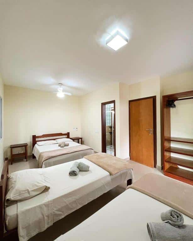 Quarto do Itamambuca casas,suítes. Duas camas de solteiro do lado esquerdo, de frente a porta do quarto e um guarda-roupa. No fundo uma cama de casal com uma mesa de apoio de cada lado, no lado direito a porta do banheiro.