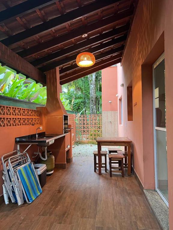 Quintal do Itamambuca casas,suítes. Do lado direito cadeiras de praia fechadas, uma pia com um gás em baixo e a churrasqueira. Do lado direito a porta da casa, uma mesa com bancos de madeira e no fundo uma ducha.