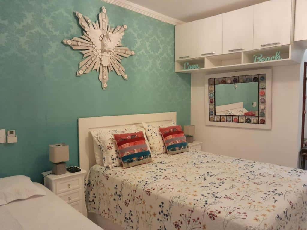 Um dos quartos do aitbnb "Linda Casa Condomínio Maresias". Duas camas estão lado a lado, separadas por uma pequena mesinha com abajur. Na parede lateral há um espelho e um armário pendurado. Este é um dos airbnb em Maresias.