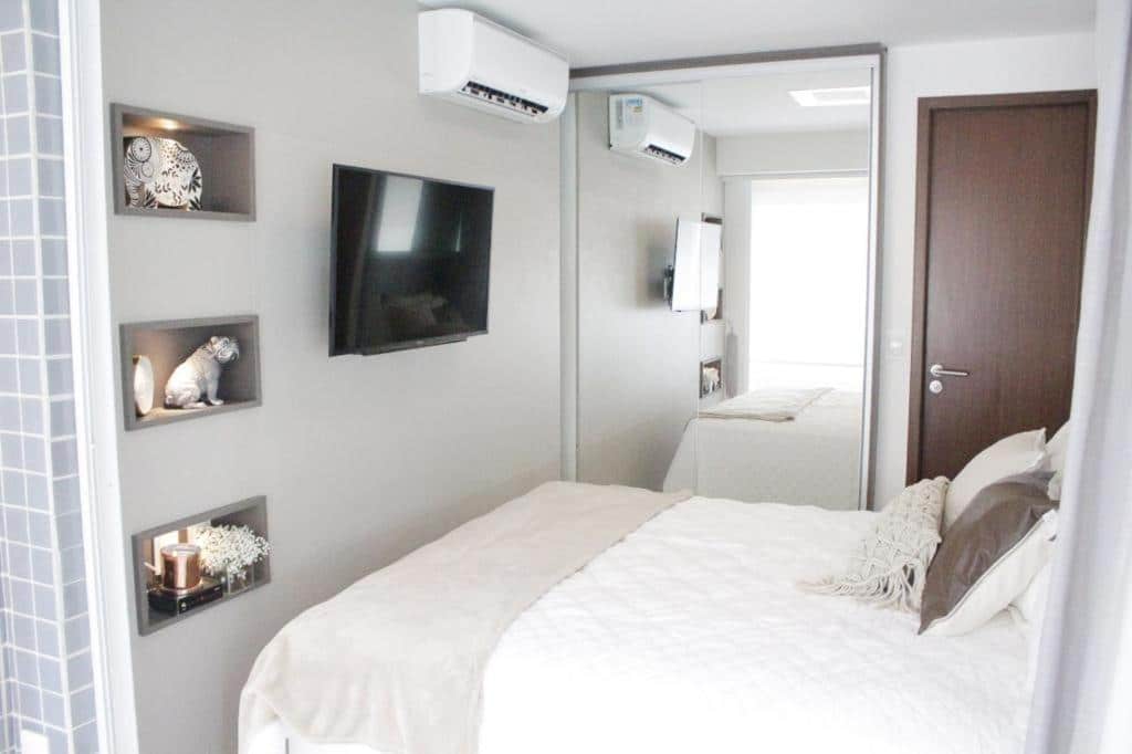 Quarto do airbnb LIV INN Apartamento na Beira-Mar Fortaleza. Uma cama de casal está no meio, de frente para uma tv e ao lado de um espelho e uma porta.