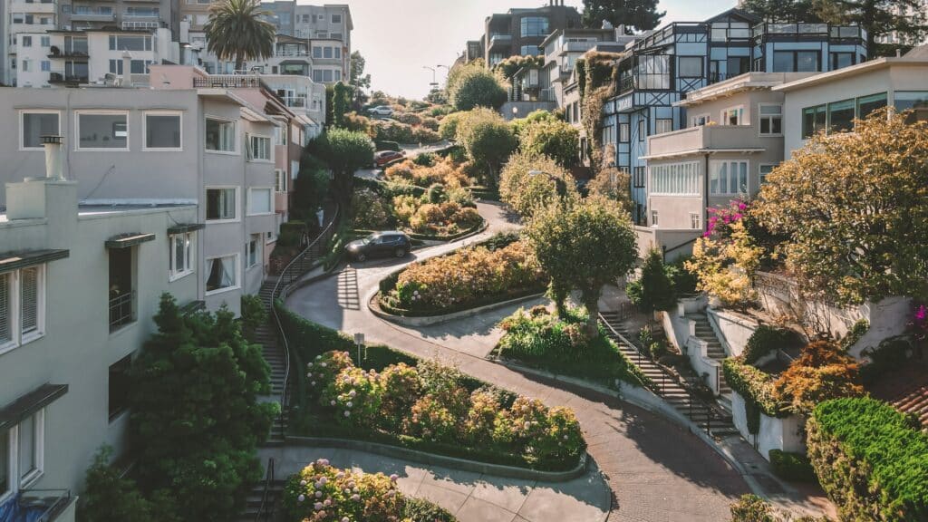 Imagem de cima da Lombard Street em San Francisco com apartamentos nos dois lados da imagem e no centro uma rua com curvas em volta de jardim.