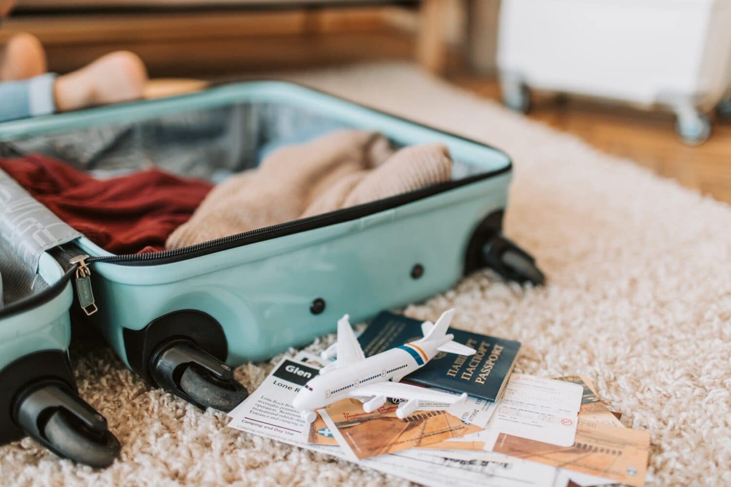 Mala de viagem sendo montada no chão, com roupas e documentos separados, além de uma miniatura de avião em cima de um mapa, para ilustrar o post de seguro viagem gratuito