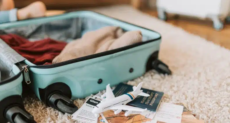 Mala de viagem sendo montada no chão, com roupas e documentos separados, além de uma miniatura de avião em cima de um mapa, para ilustrar o post de seguro viagem gratuito