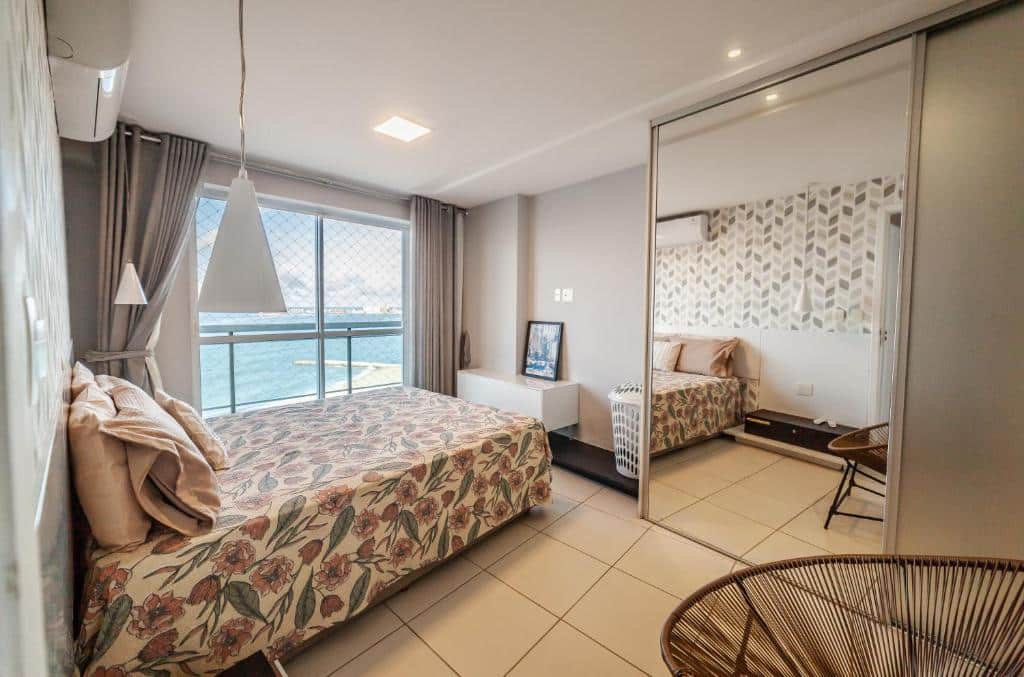 Quarto do Modern Beachfront Apartment w. Magnificent Seaview. Uma cama de casal está ao lado da janela, que possui vista para o mar. Do outro lado da cama está um armário com um grande espelho e uma cadeira. Este é um airbnb em Fortaleza.