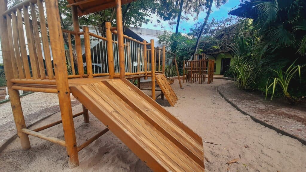 Parquinho do Ritz lagoa da Anta, com dois playgrounds de madeira com escorredor, balanço e árvores em volta. O chão é com areia