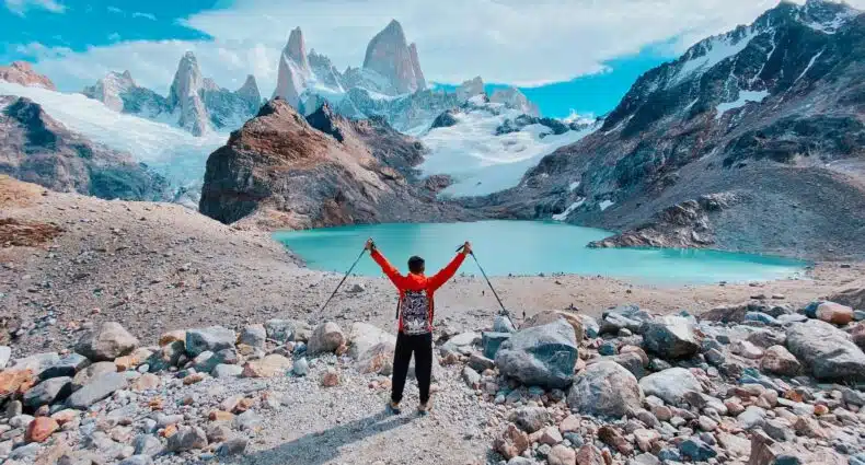 Um homem com roupas de esqui parado em frente há um lago e montanhas nevadas na Patagônia Argentina, para representar o melhor seguro viagem América do Sul